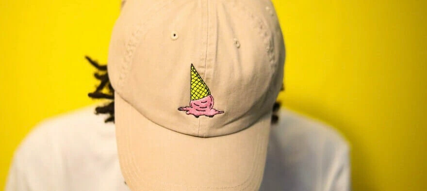 A beige dad cap with a melting ice cream cone embroidered on the front, worn by a person against a yellow background.