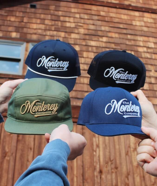 holding up four custom monterey company hats