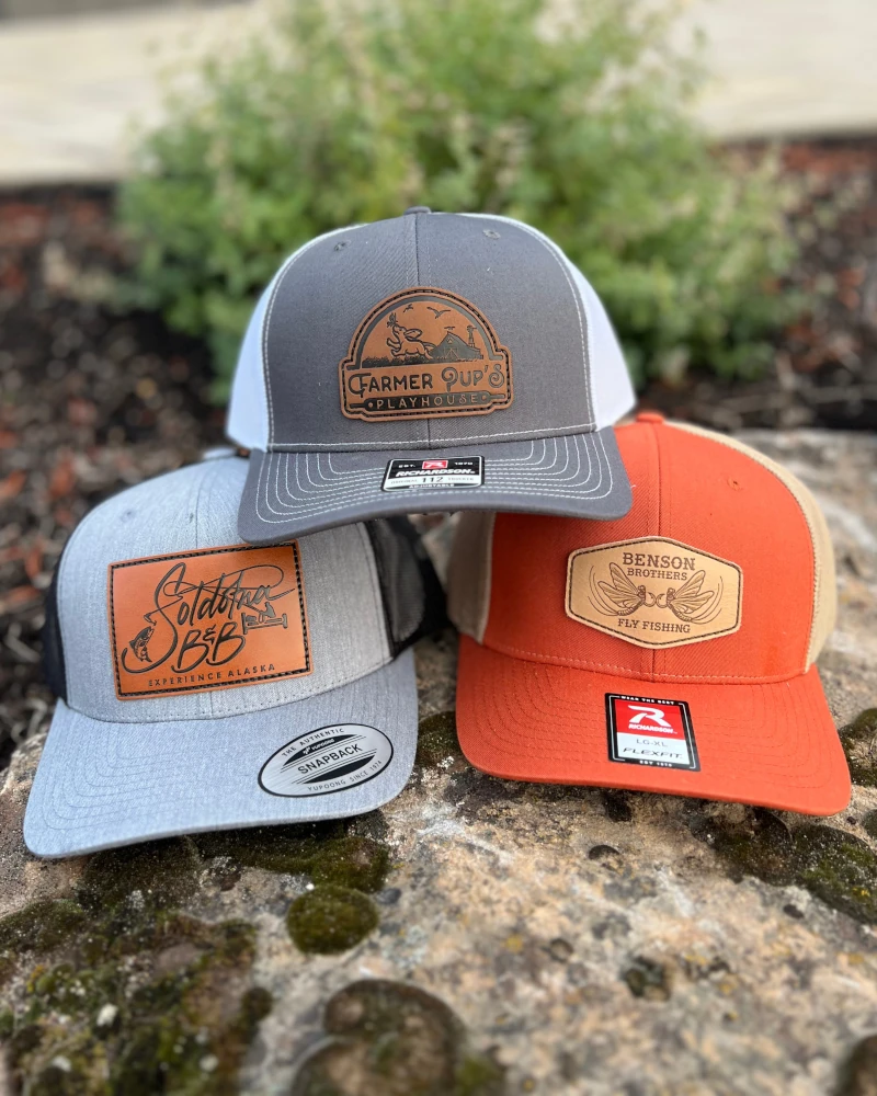 three hats with custom leather patches on them sitting on rock
